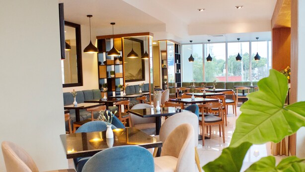 A modern restaurant with a mix of seating options, including tables and booths, and a large window offering a view of the outdoors. - Habitat Hotel (Lima)