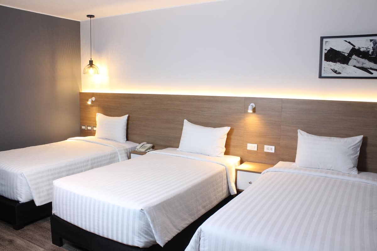 Hotelkamer met twee enkele bedden, een houten hoofdbord, bedlampjes, een telefoon en een lijst aan de muur.
