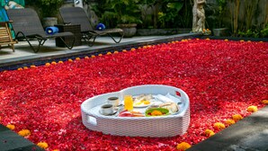 A breakfast tray on a bed of red flower petals with a statue and chairs in the background. - Villa Bakti Ubud (Ubud)