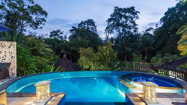 A swimming pool with a curved edge, surrounded by lush greenery and a gazebo. - Villa Bakti Ubud (Ubud)