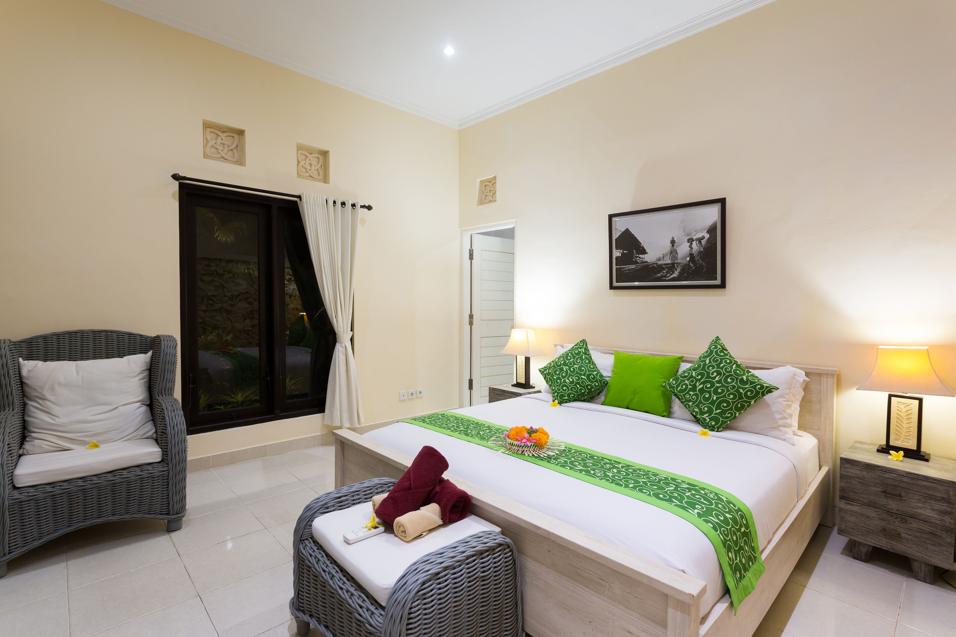 A hotel room with a bed, two chairs, a nightstand, a lamp, and a picture on the wall.