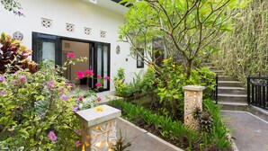 A white building with a black door and windows, surrounded by lush greenery and flowering plants. - Villa Bakti Ubud (Ubud)