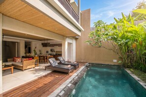 Een modern zwembad met loungebedden, een houten terras en uitzicht op de leefruimte.