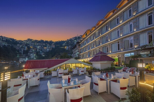 A rooftop restaurant with outdoor seating, overlooking a cityscape at dusk. - Snow Valley Resorts (Shimla)