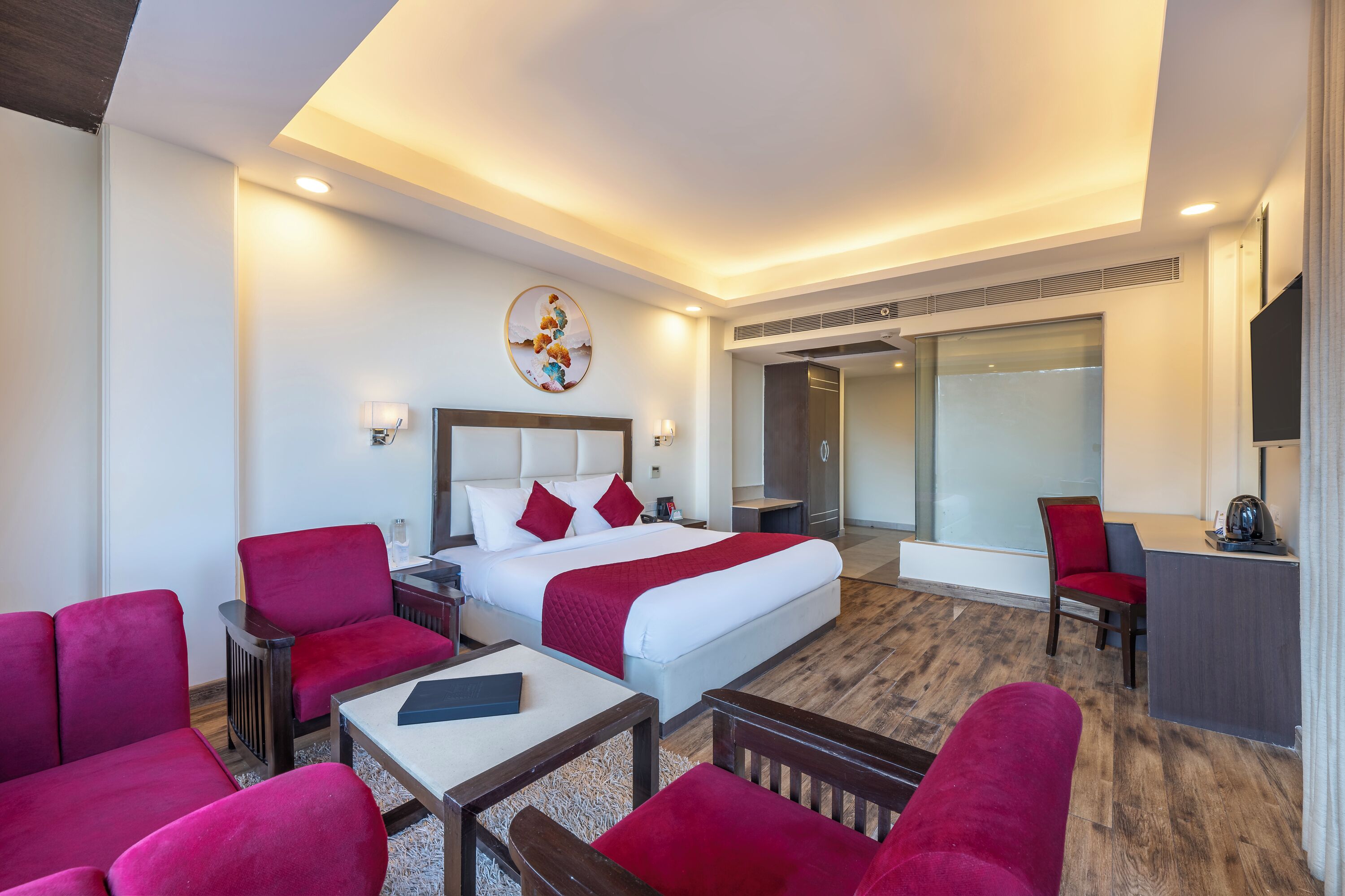 A hotel room with a bed, red upholstered chairs, a desk, and a television.