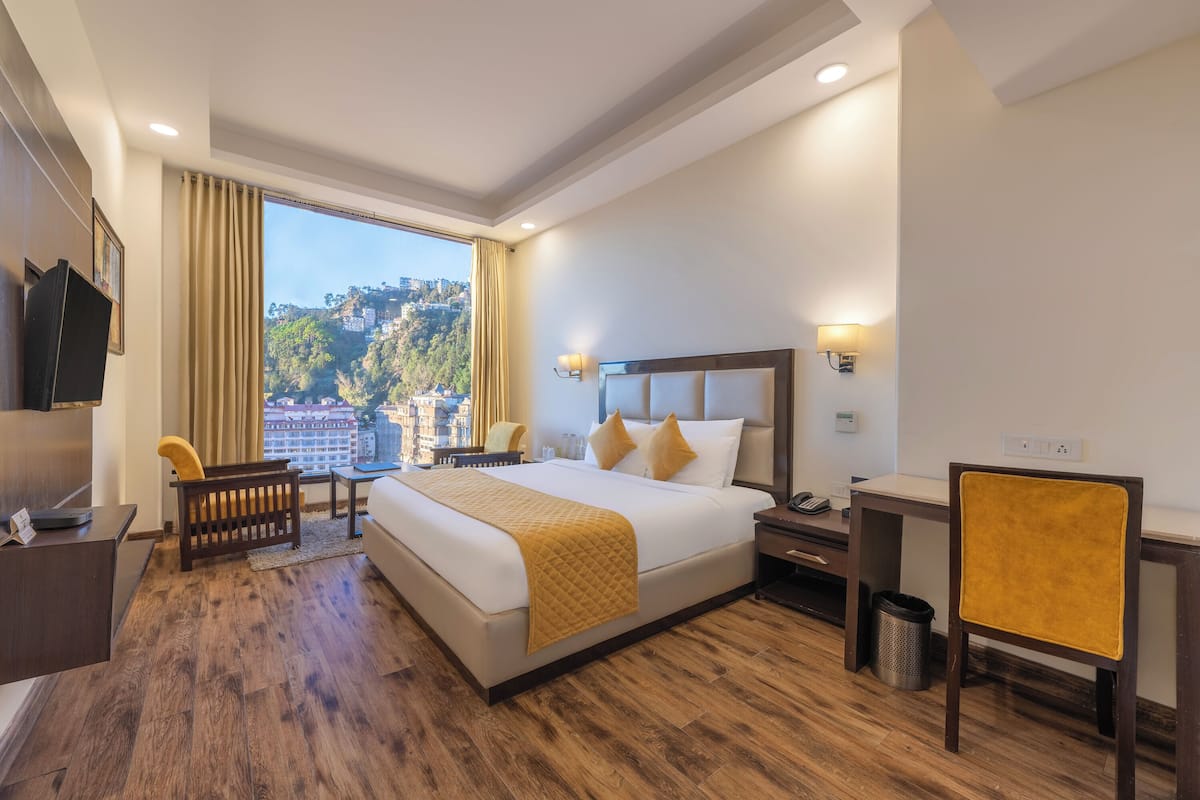 Habitación de hotel con una cama grande, un escritorio, una silla y vistas a un paisaje urbano.