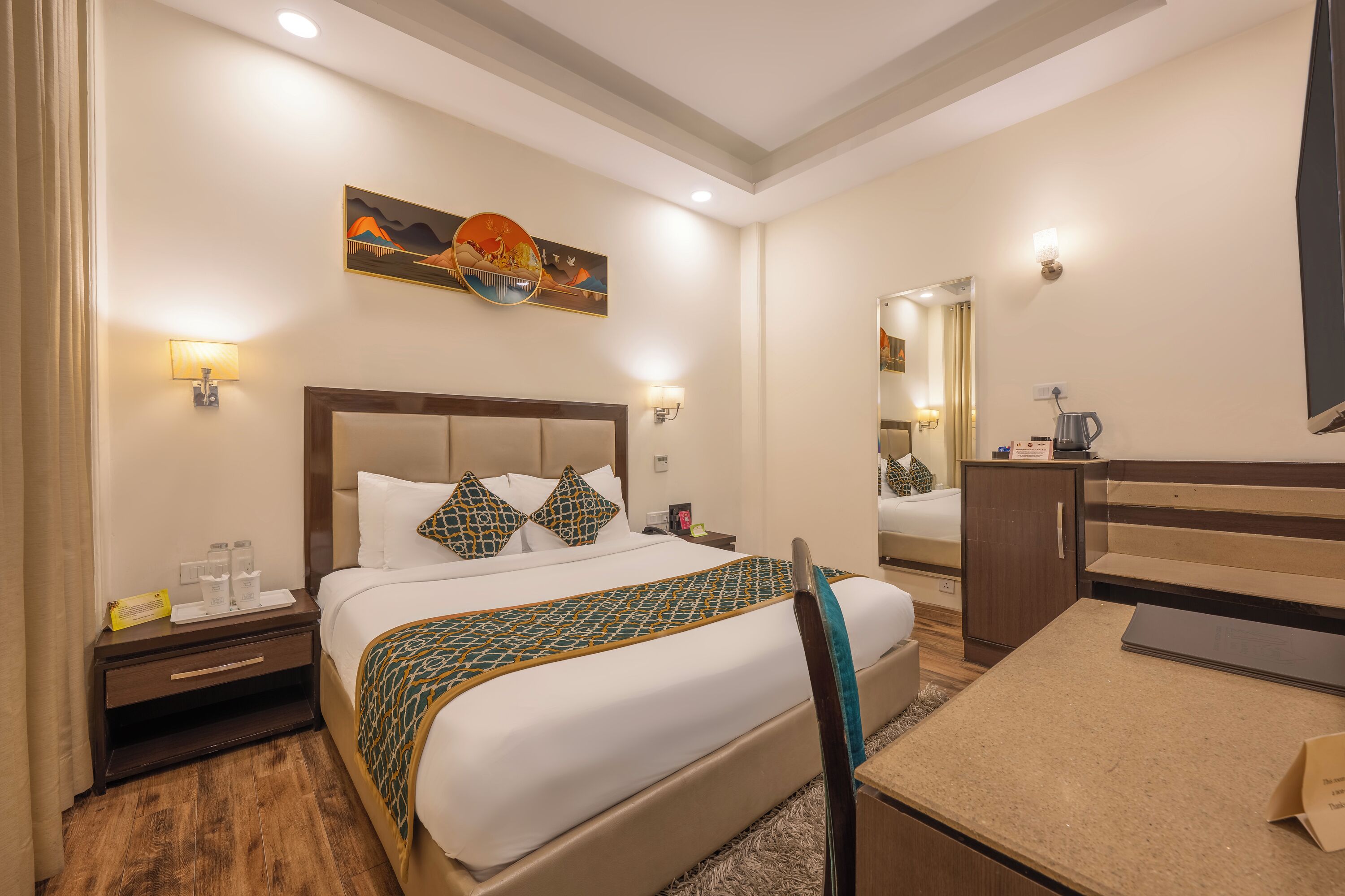 Une chambre d’hôtel comprenant un lit, des tables de chevet, un bureau, une chaise, un miroir et un tableau au mur.