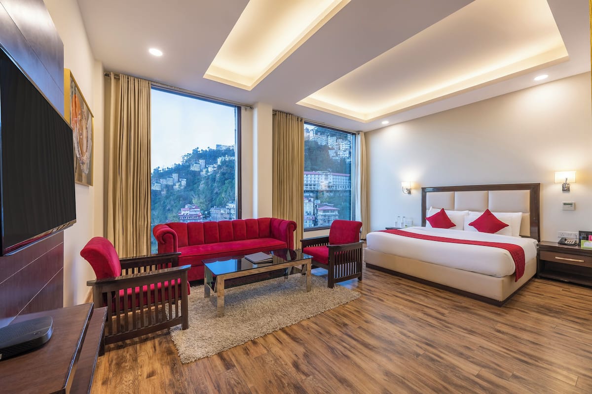 Una habitación de hotel moderna con una cama grande, un sofá rojo, un televisor y vistas a la ciudad.