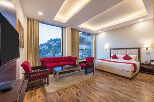 A modern hotel room with a large bed, a red sofa, a TV, and a city view.