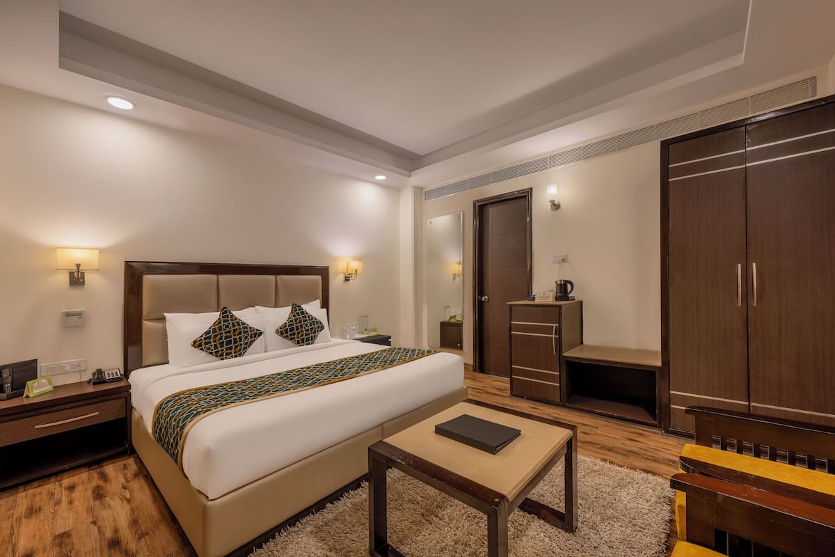 Una habitación de hotel con una cama grande, mesitas de noche, un armario y una pequeña mesa.