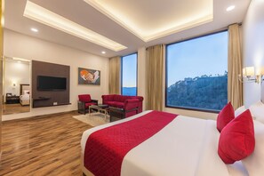 A modern hotel room with a large bed, a TV, a seating area, and a view of the outdoors. - Snow Valley Resorts (Shimla)