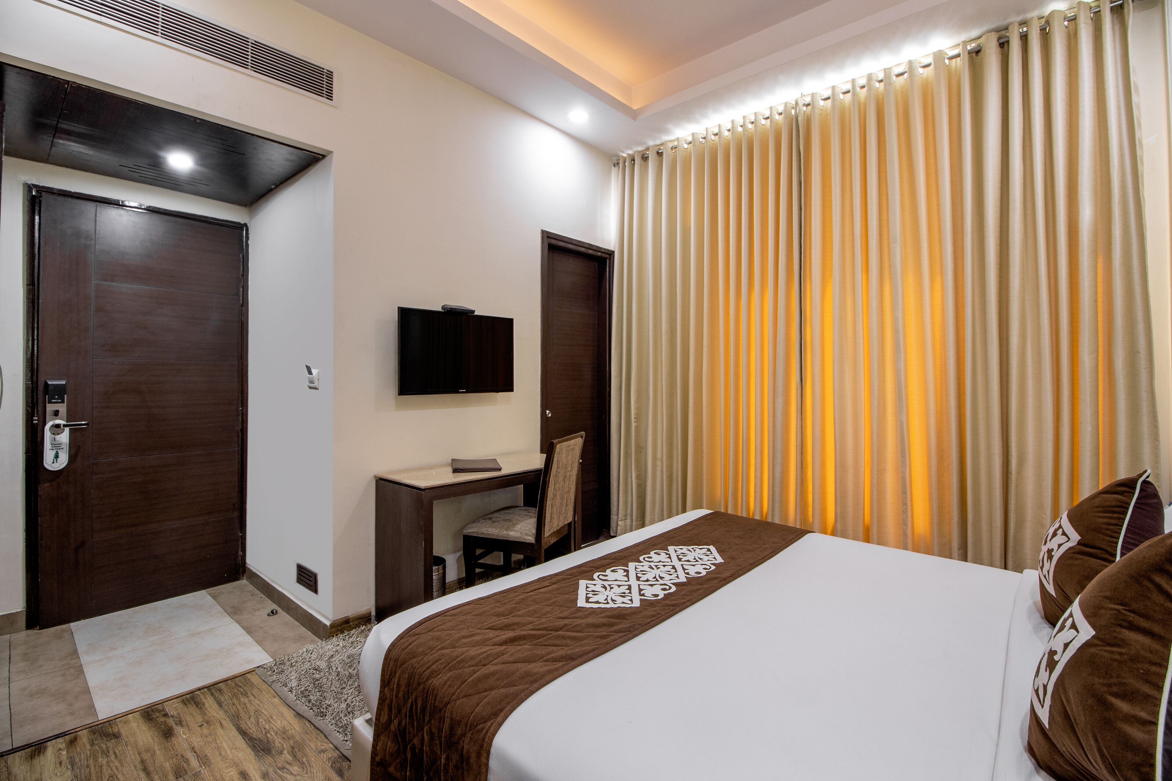 A hotel room with a bed, a desk, a chair, a television, and a window with curtains.