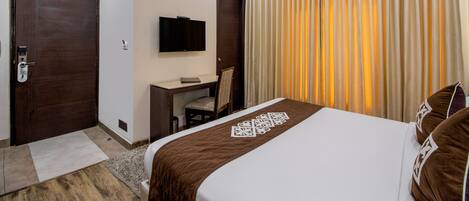 A hotel room with a bed, a desk, a chair, a television, and a window with curtains.