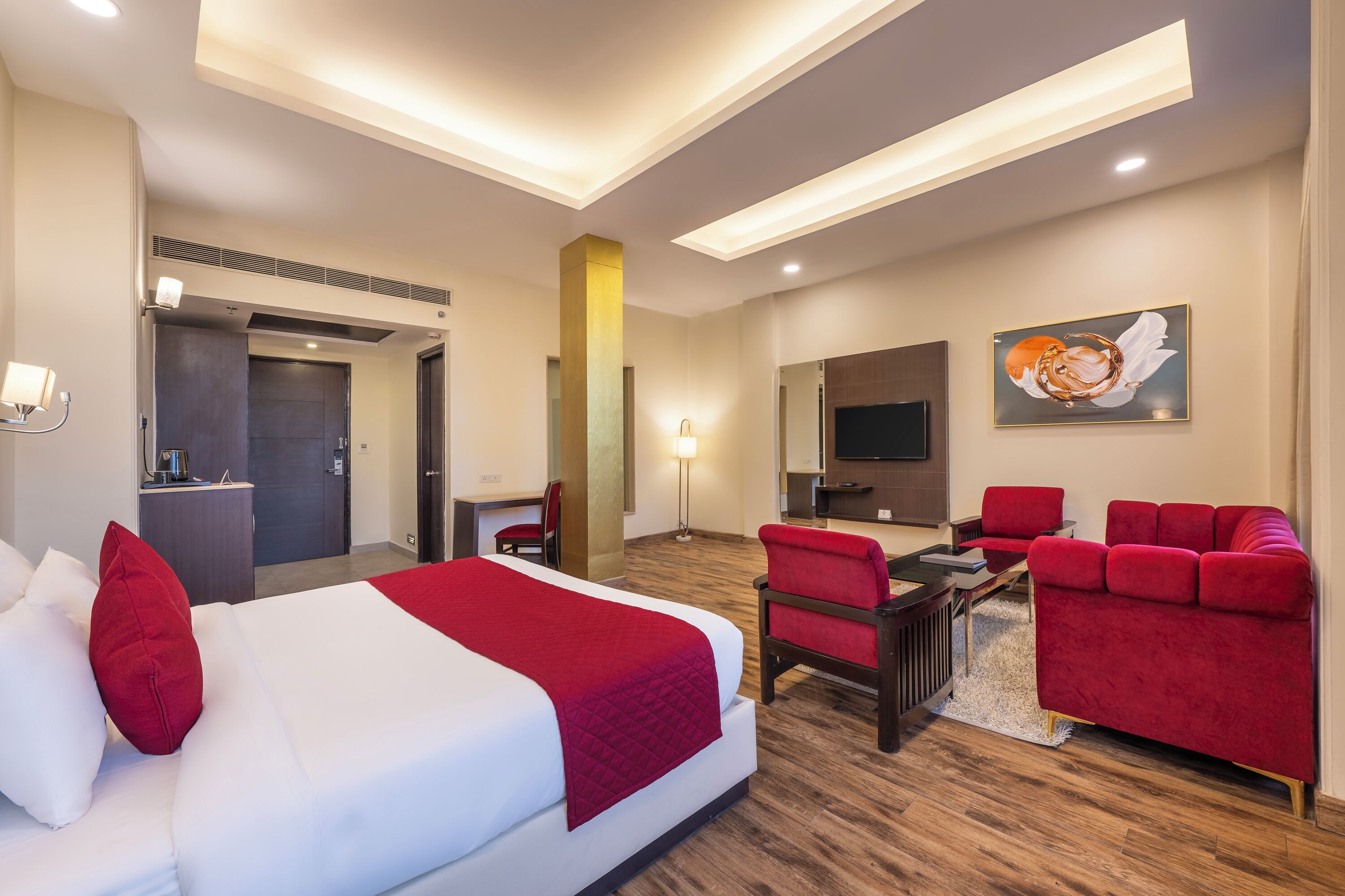 A hotel room with a large bed, red upholstered chairs, a small table, a TV, and a painting on the wall.