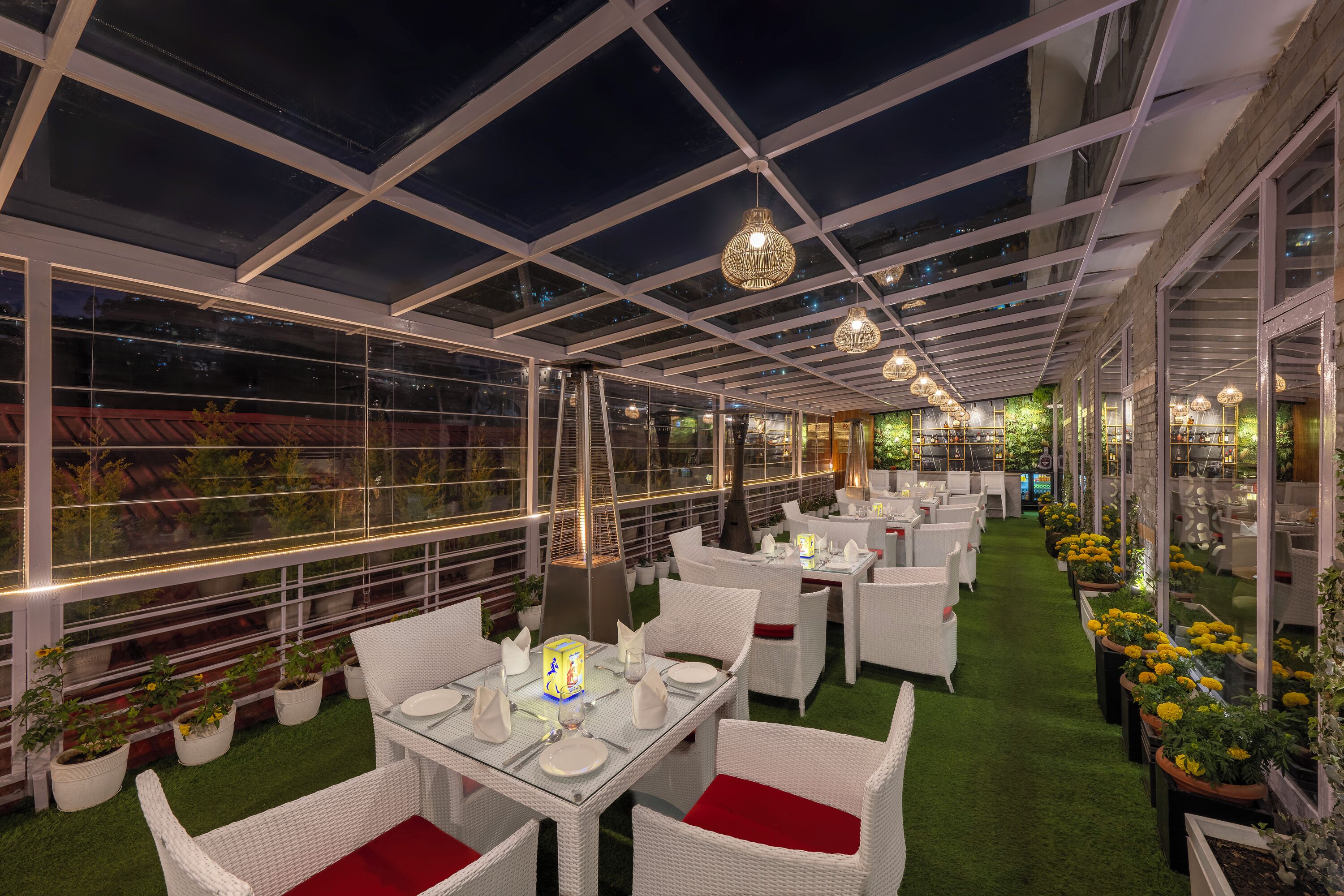 An indoor garden restaurant with tables and chairs, glass ceiling, and potted plants.