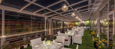 Un restaurant aménagé comme un jardin intérieur, avec des tables, des chaises, un plafond en verre et des plantes en pot.