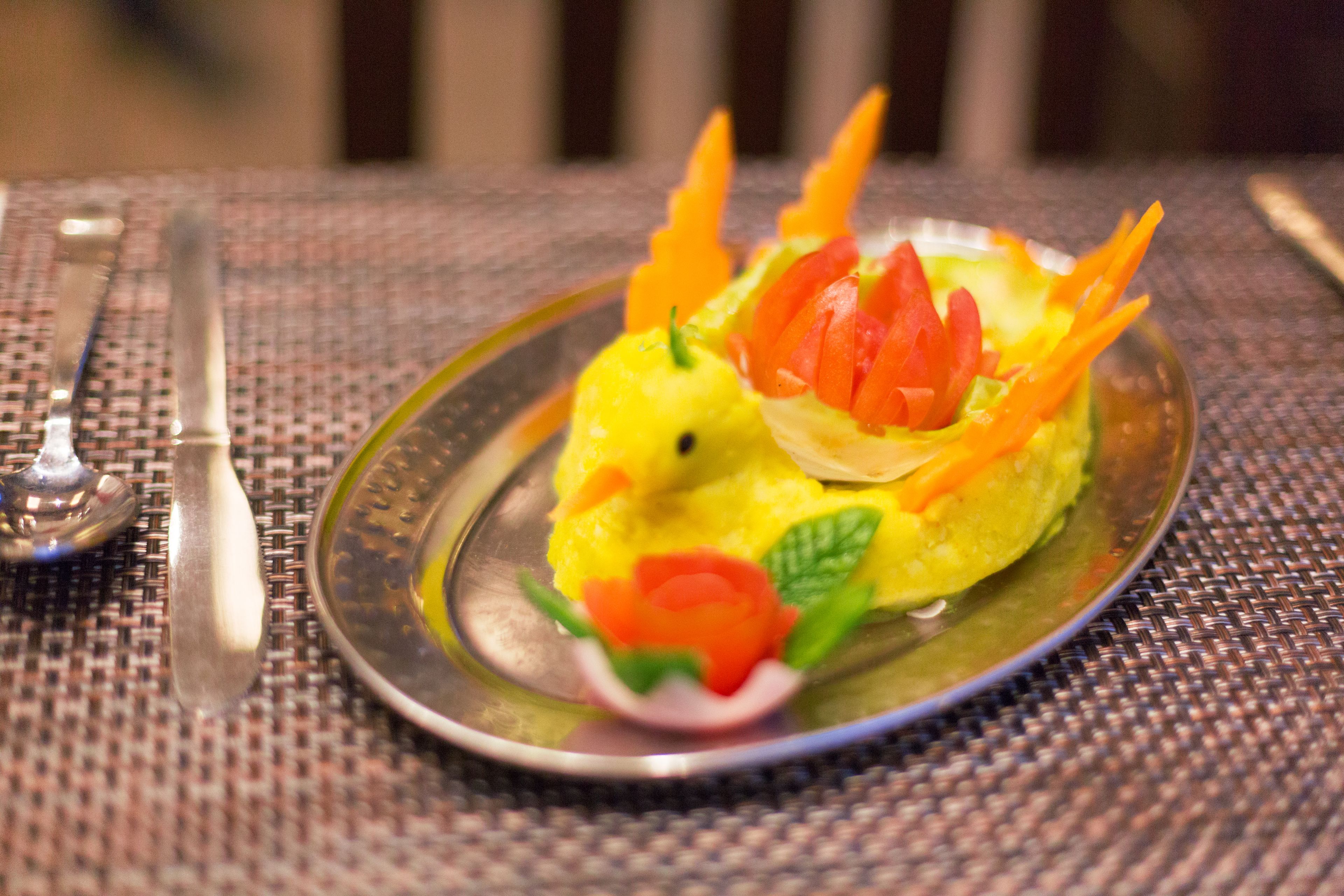 Ein Teller mit einer ansprechend platzierten Speise, möglicherweise Gemüse oder Obst, garniert mit Karotten- und Tomatenscheiben.