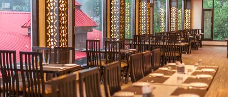 A restaurant with multiple tables and chairs, large windows, and decorative panels.