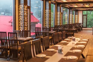 Un restaurante con varias mesas y sillas, ventanas amplias y paneles decorativos.