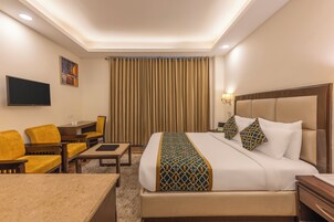 A hotel room with a large bed, a desk, a chair, and a television on the wall.
