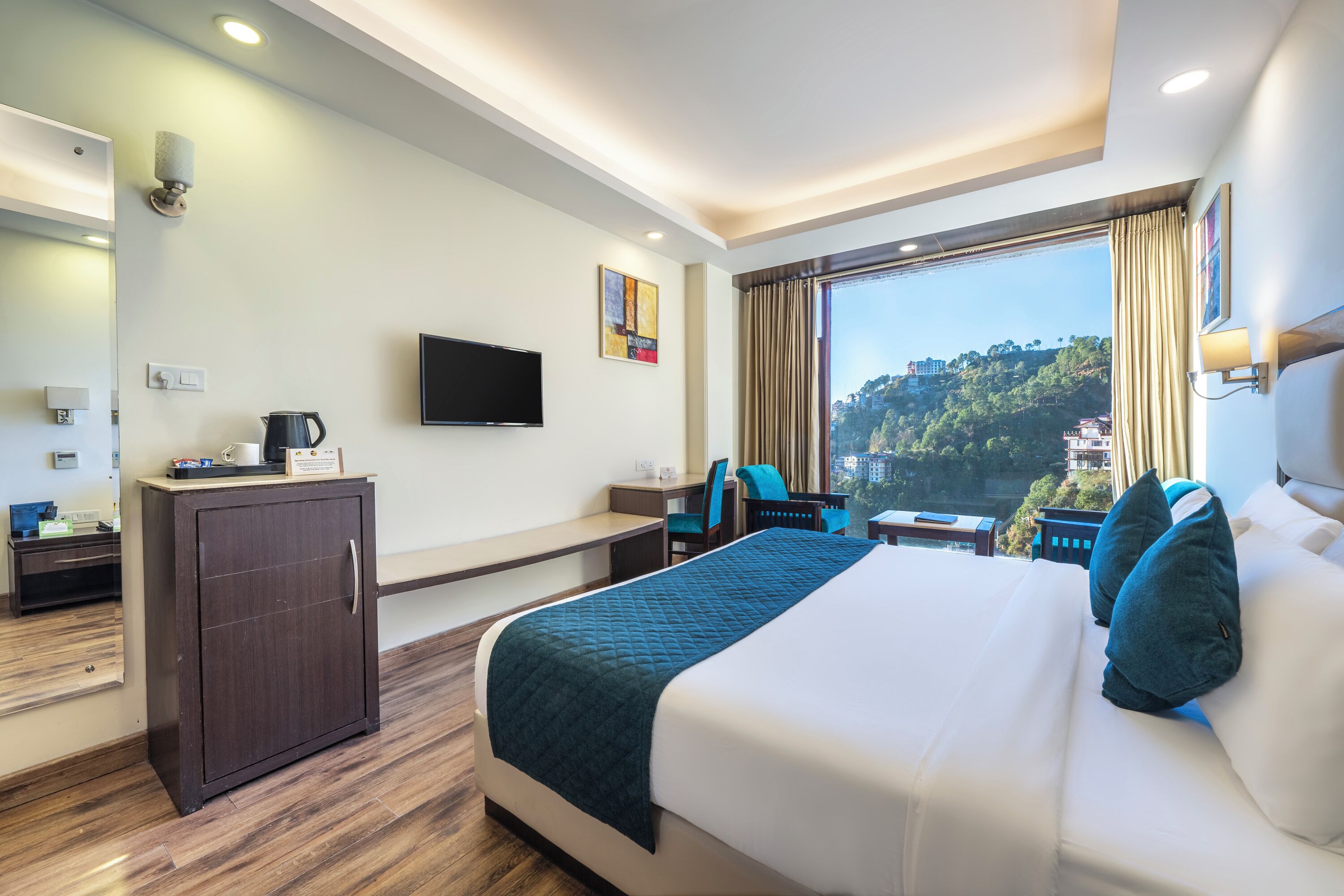 A hotel room with a bed, a desk, a chair, a television, and a view of a mountainous landscape.