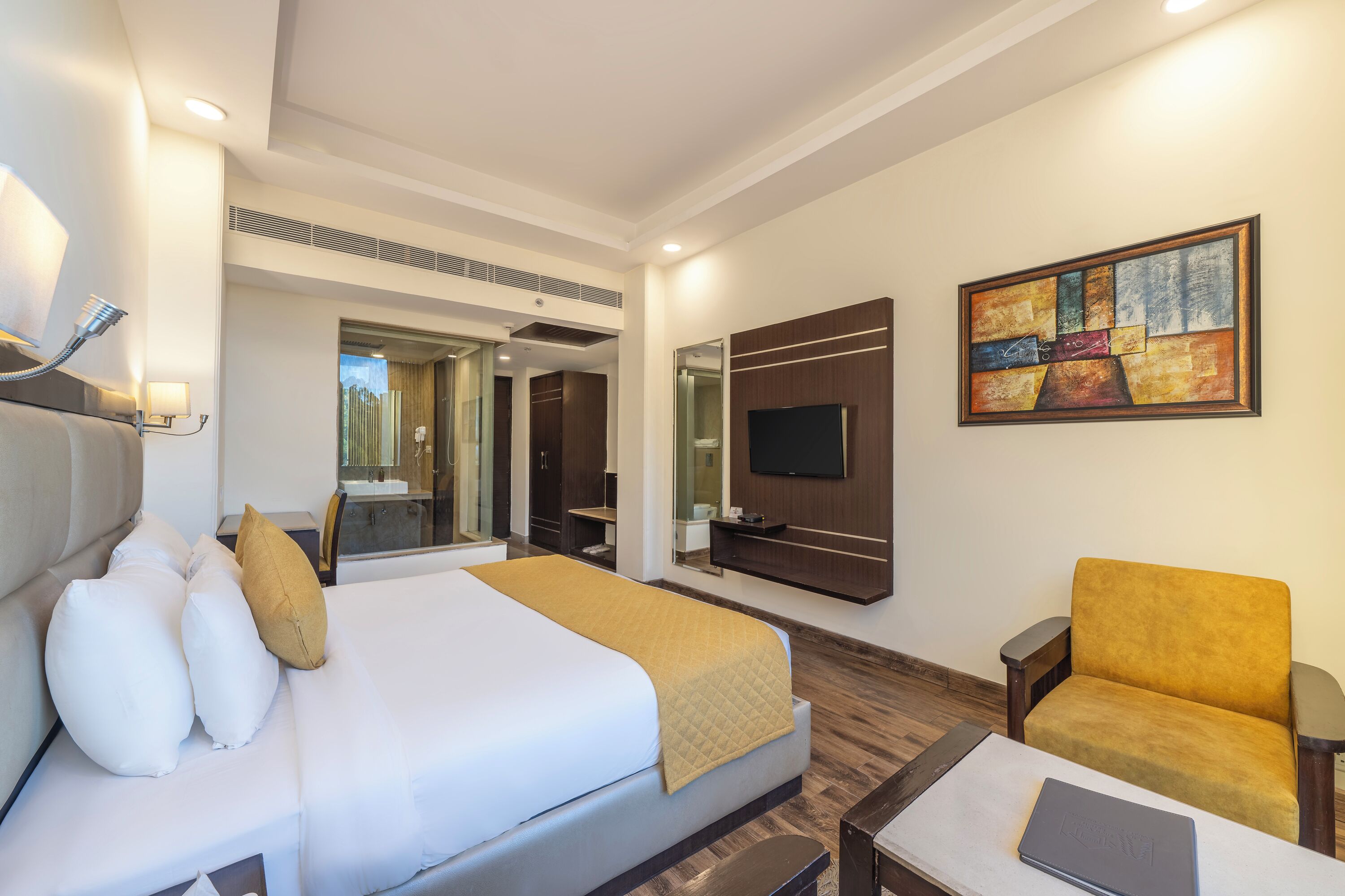 A hotel room with a bed, a chair, a desk, a TV, and a painting on the wall.