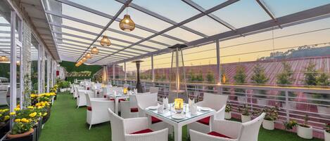 An outdoor dining area with white wicker furniture, green artificial turf, and potted plants.