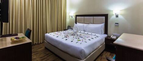 Una habitación de hotel con una cama grande, un escritorio con una cesta de fruta, un televisor y una mesita de noche con un teléfono.