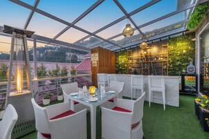 Een terras met een eettafel, witte rieten meubels en een groene wand vol planten.