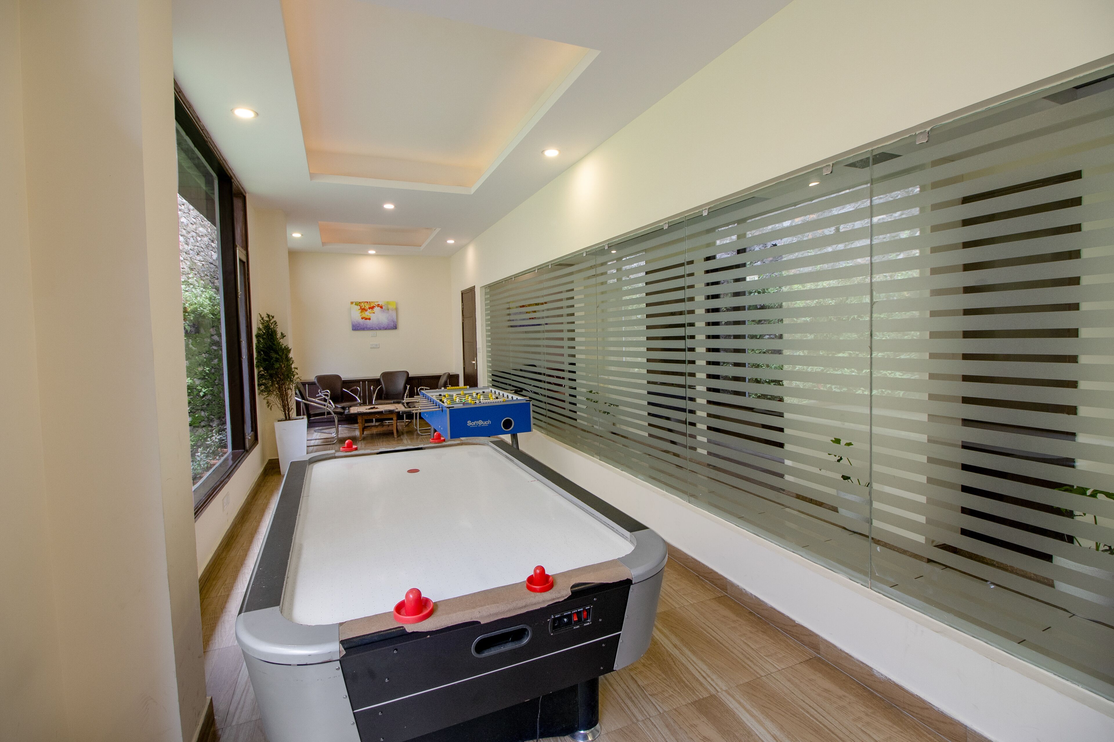 A pool table with a foosball table and a foosball table in a room with large windows and blinds.