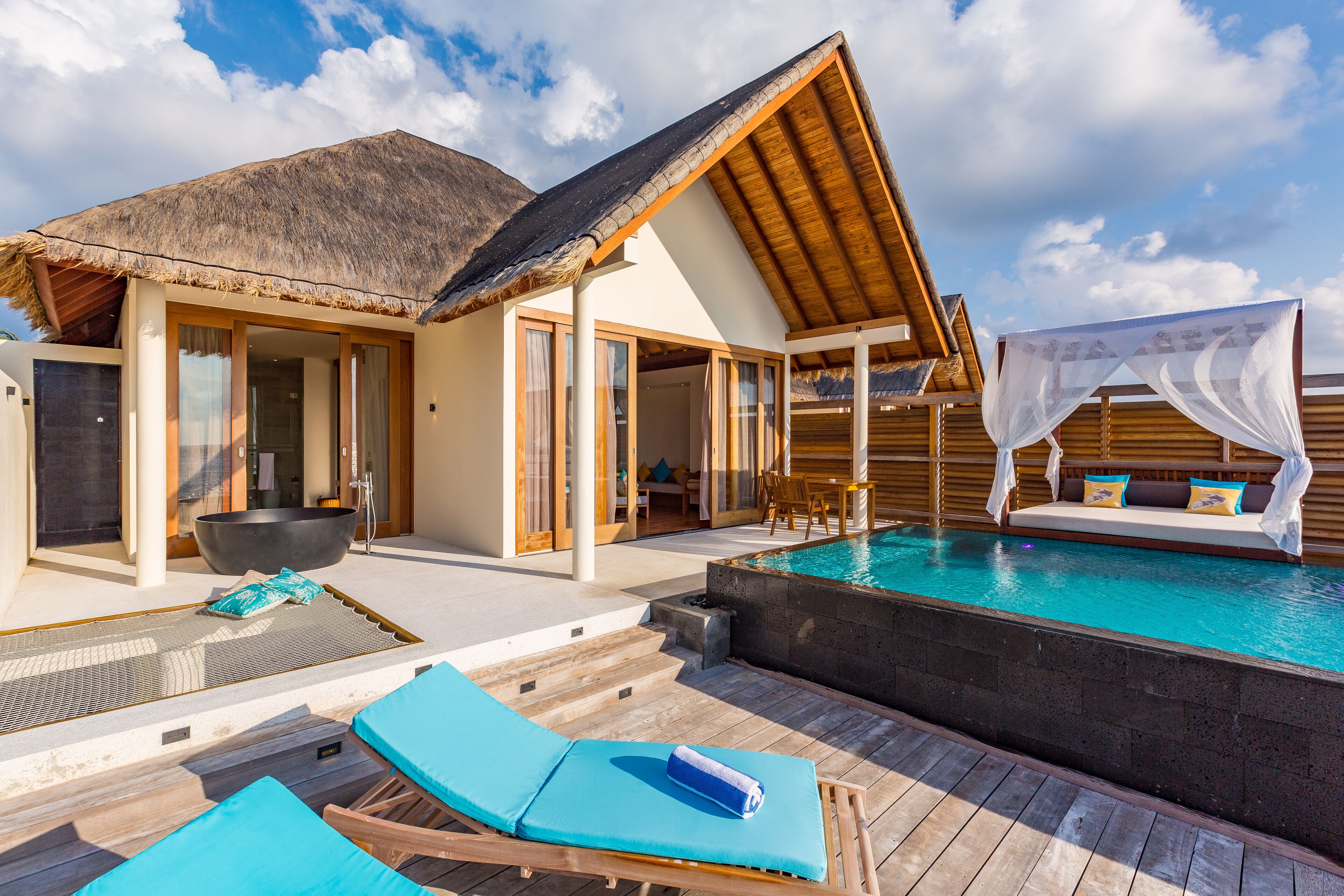 A poolside area with lounge chairs, a hot tub, and a thatched-roof structure.