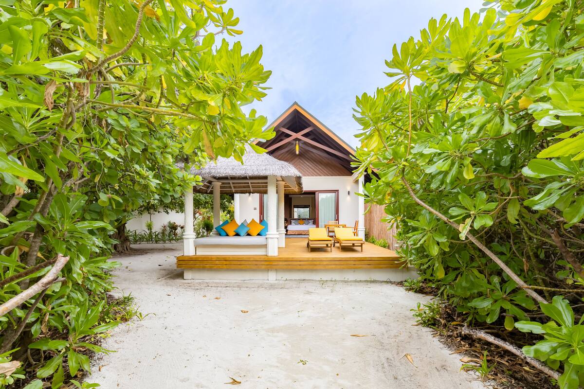 A bungalow with a thatched roof, a wooden deck, and a covered seating area.
