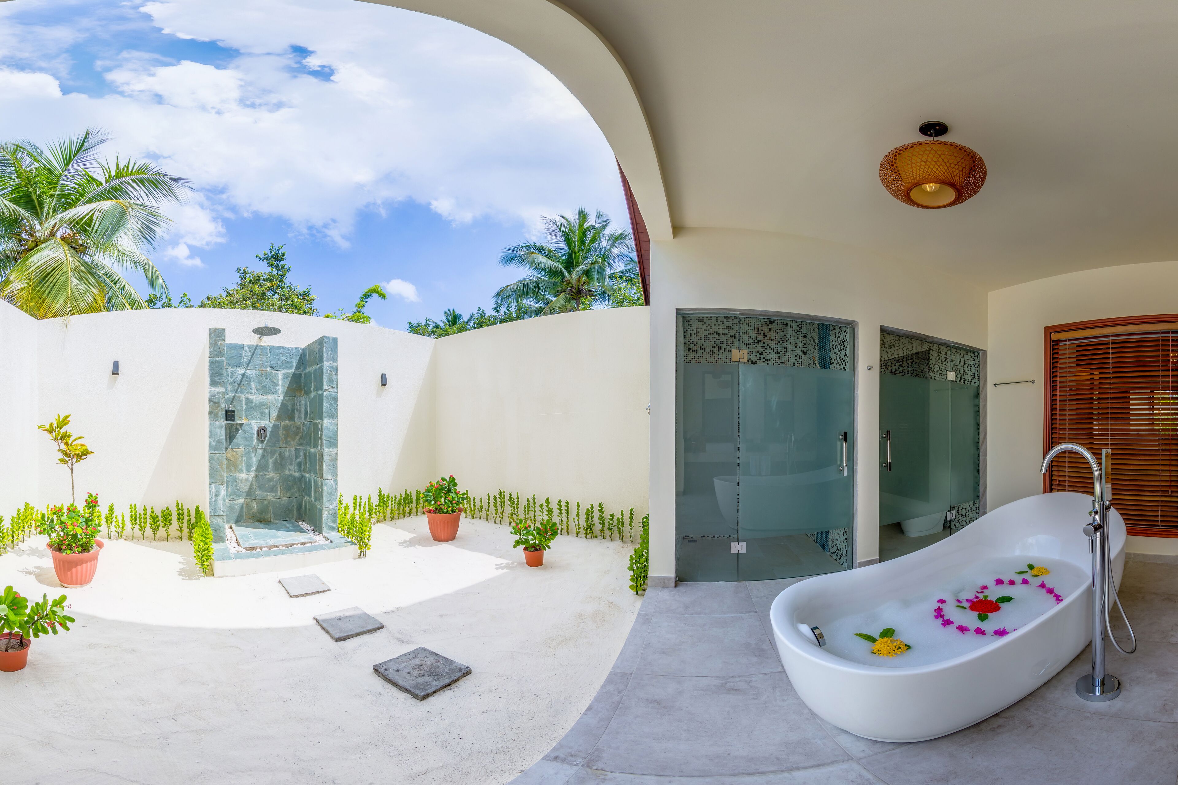 A modern bathroom with a freestanding bathtub, a glass shower enclosure, and a view of the sky and palm trees.