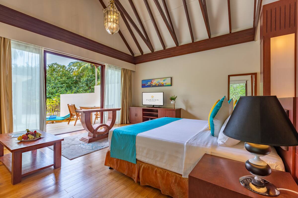 A hotel room with a bed, bedside table, lamp, TV, and a view of the outdoors.