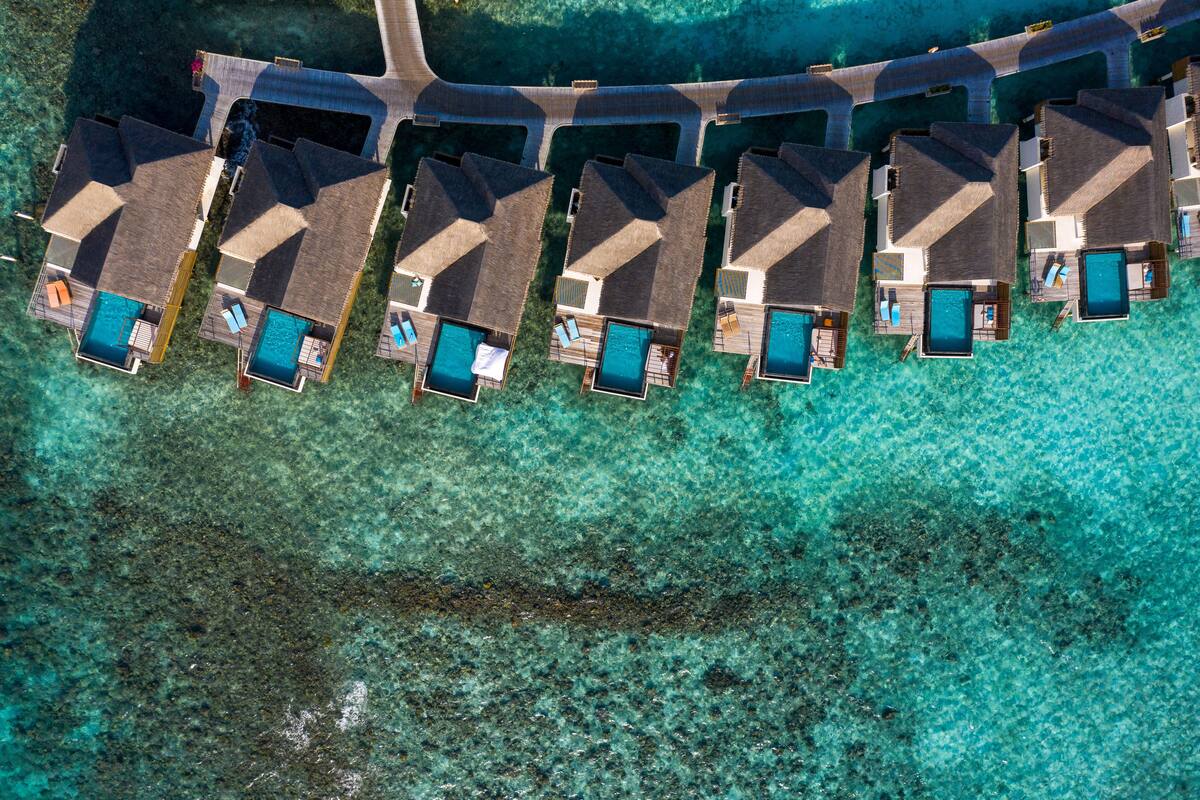 An aerial view of a resort with multiple overwater bungalows, each with a private pool and direct access to the ocean.