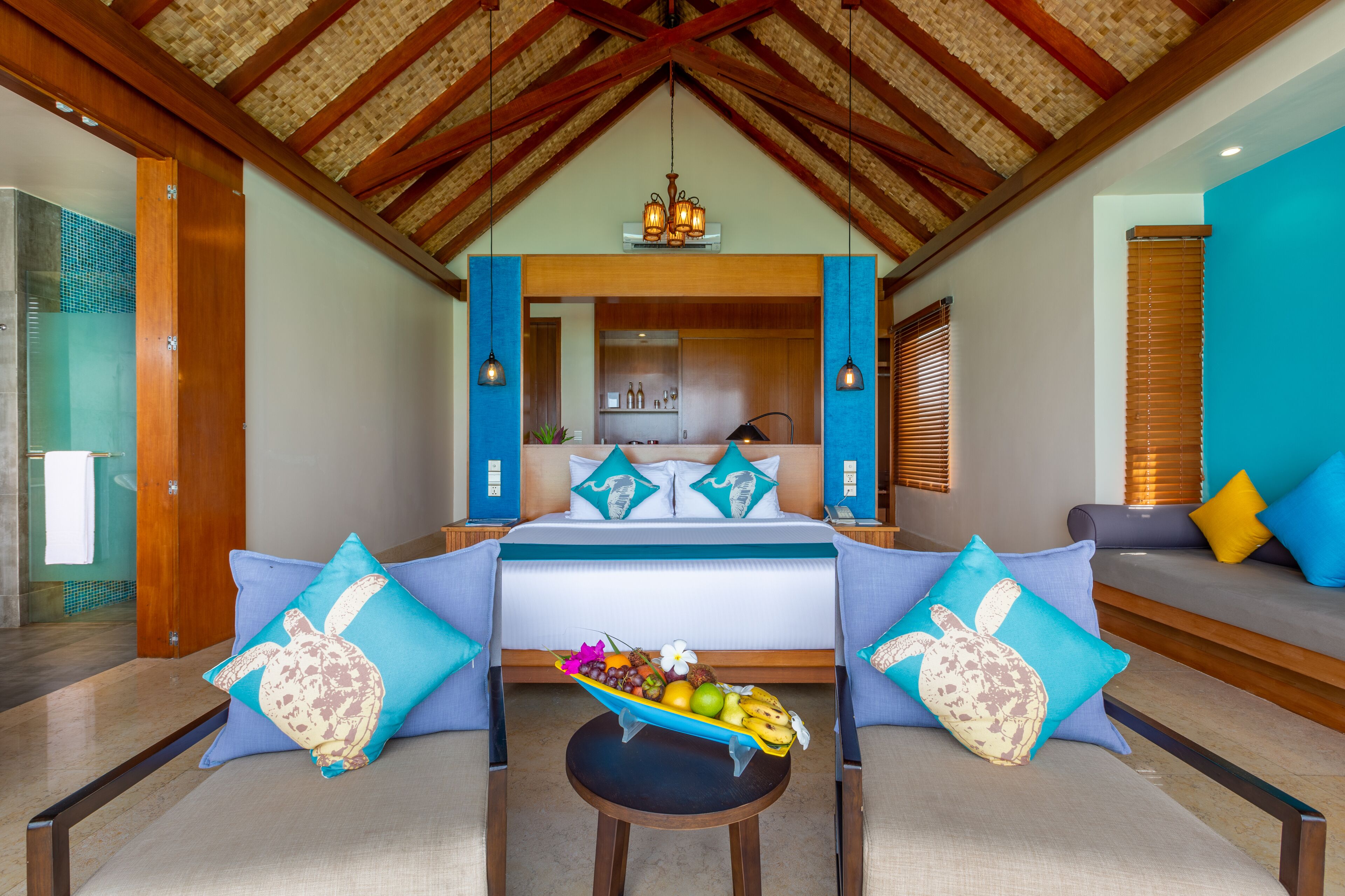 A bedroom with a bed, two sofas, a small table with fruit, and a view of a kitchen and bathroom.