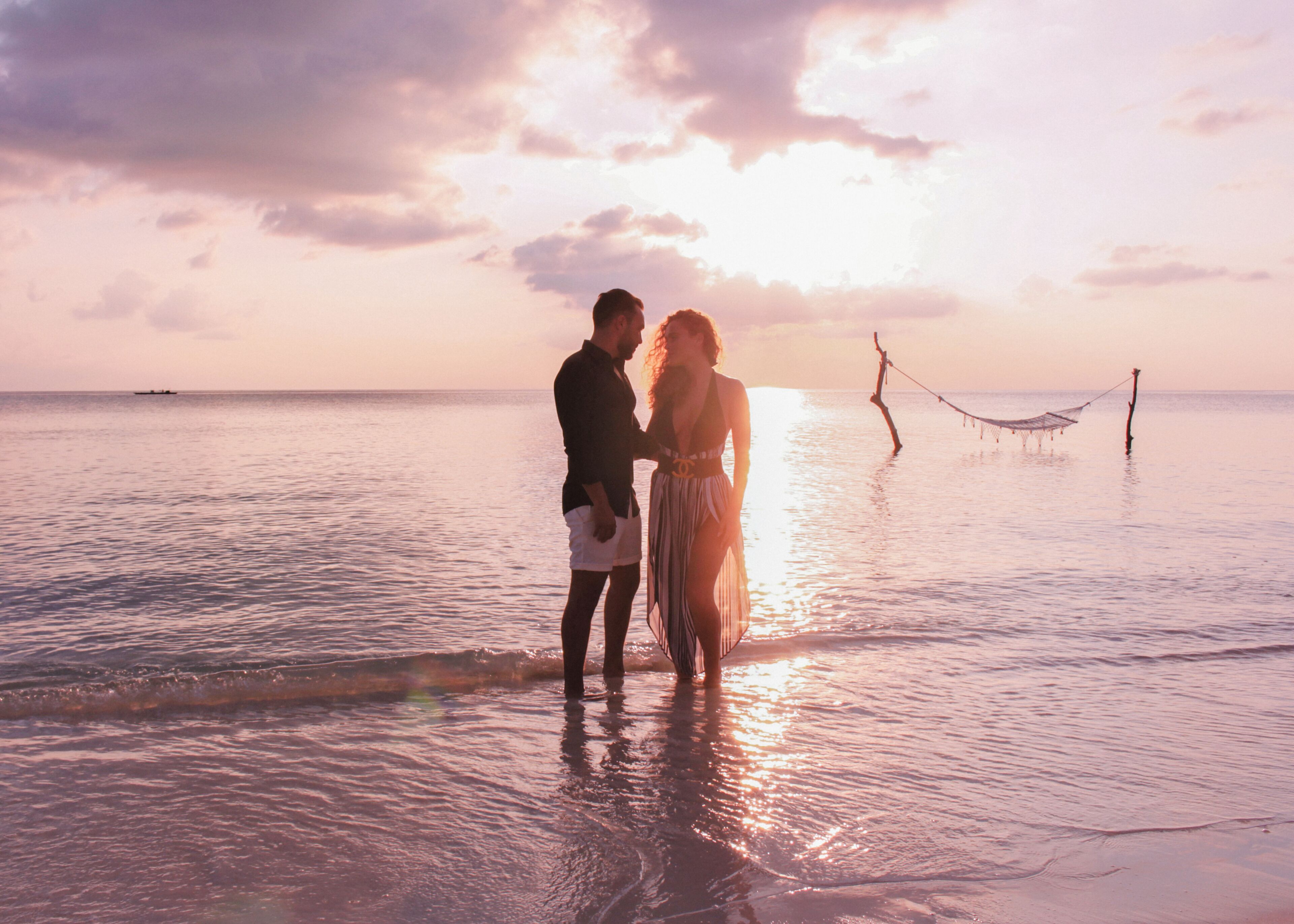 A couple standing on a beach at sunset with a hammock in the background.