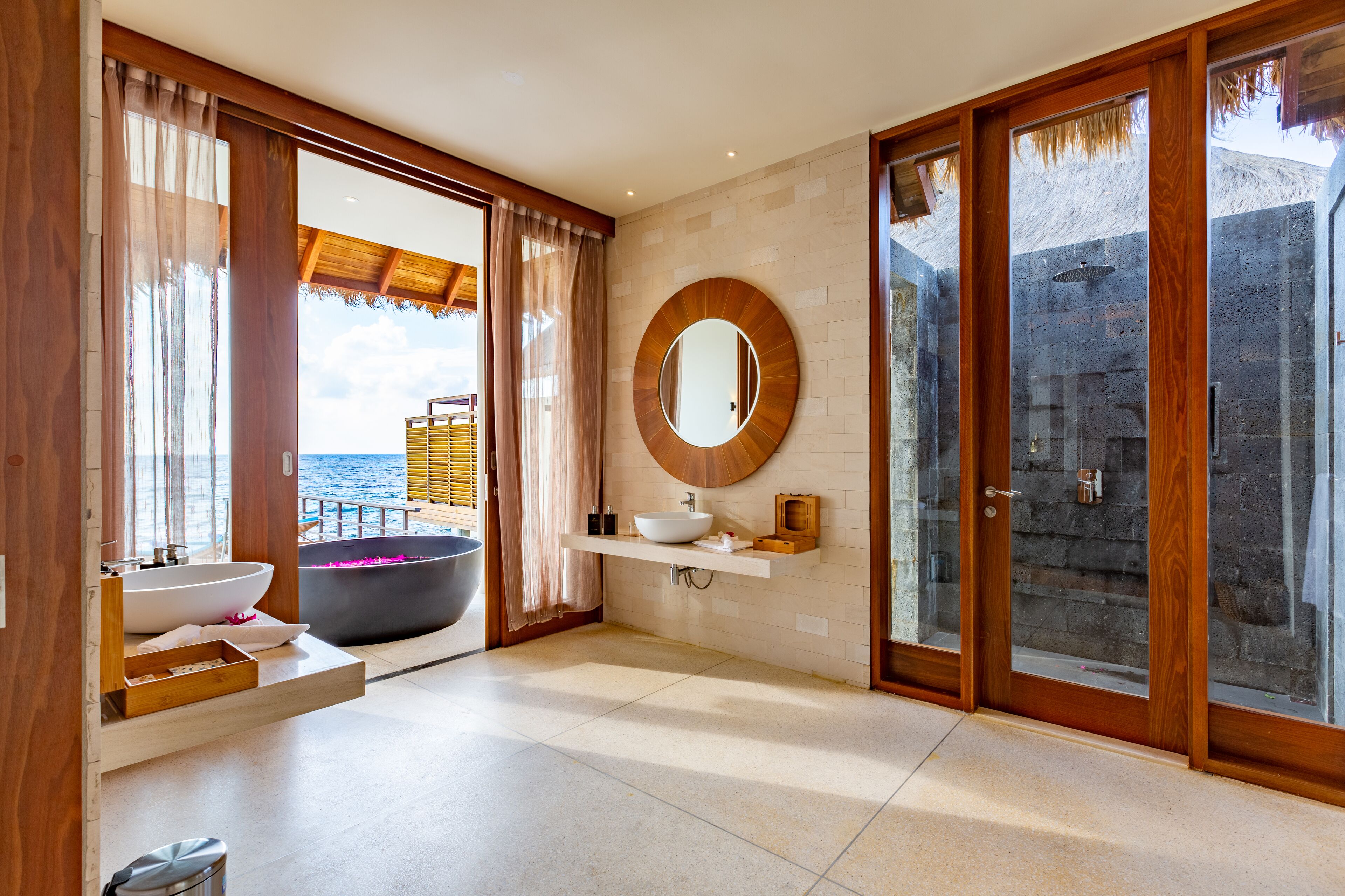 A modern bathroom with a large bathtub, a round mirror, and a view of the sea.