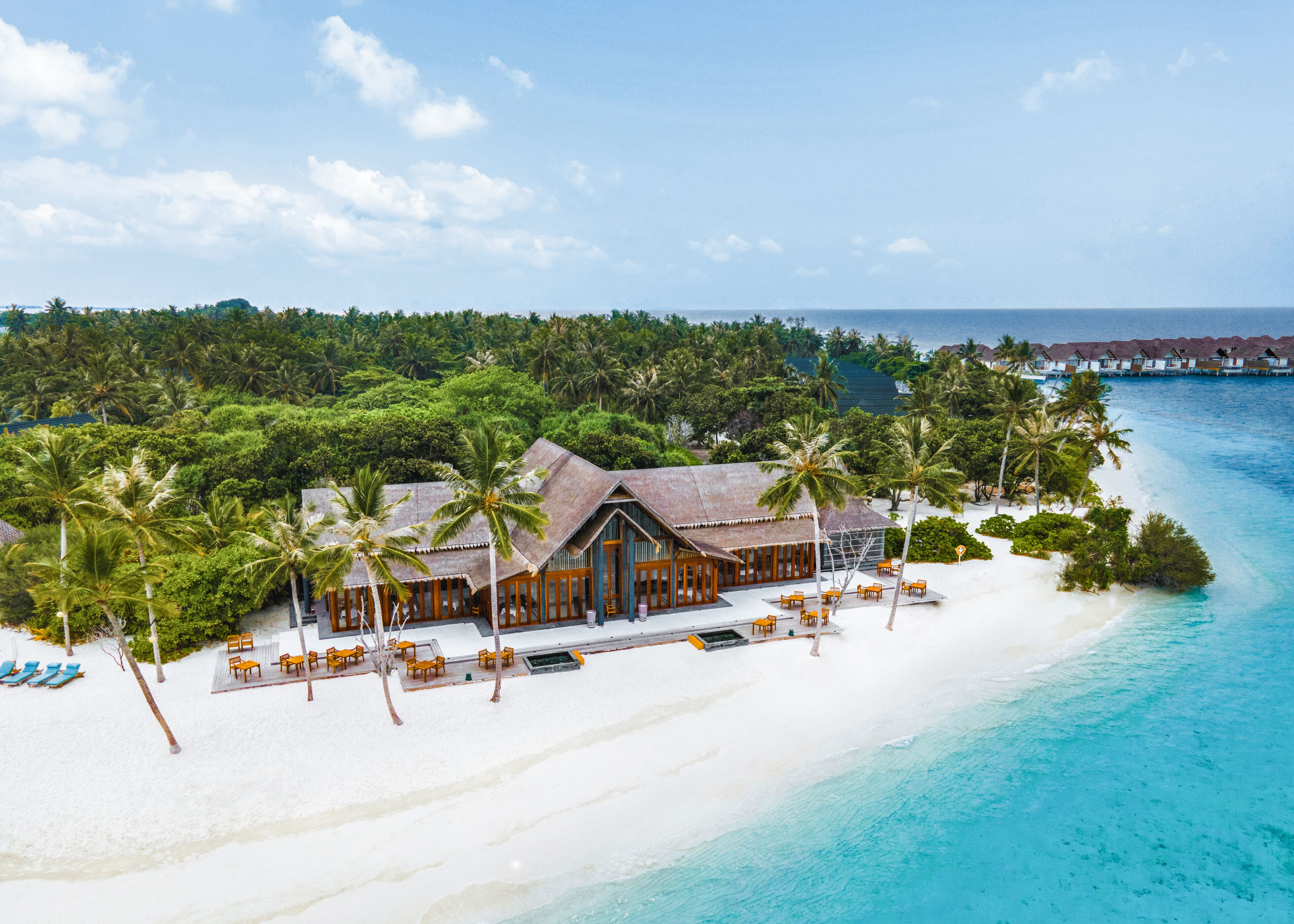 A beachfront resort with a wooden building, palm trees, and a white sandy beach.