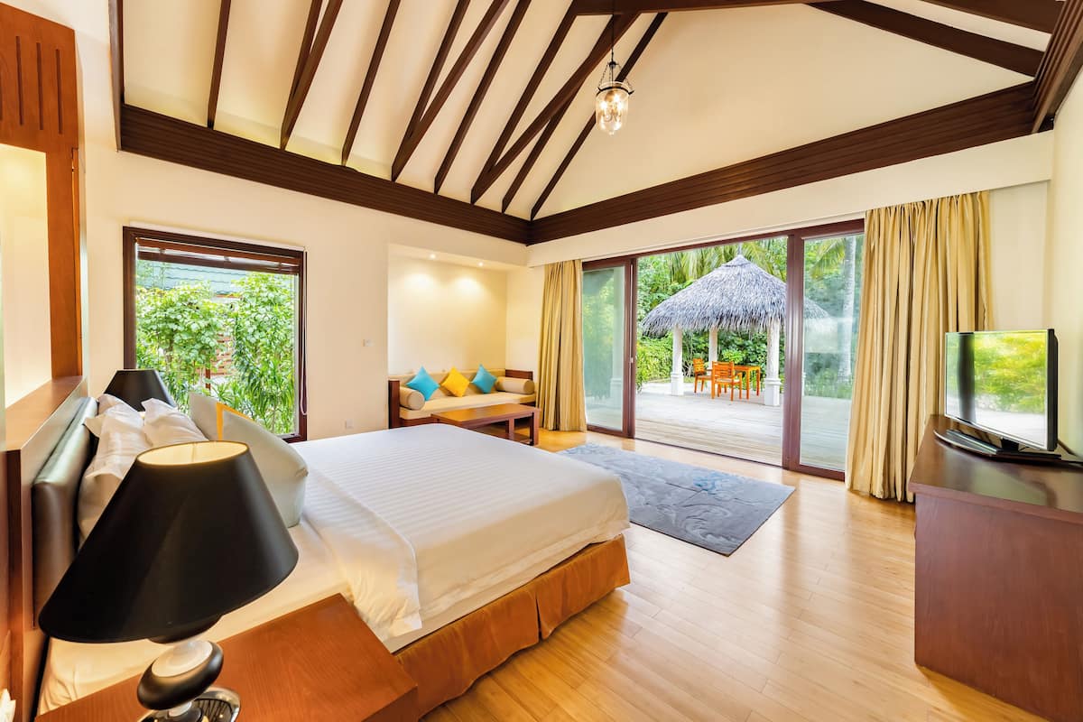 A hotel room with a large bed, a desk, a TV, and a balcony with a thatched umbrella.
