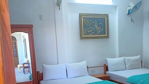 A room with two wooden beds, white bedding, a teal blanket, a framed artwork on the wall, and a wooden door. - Blue Sea 2 Hotel (Bac Nha Trang)
