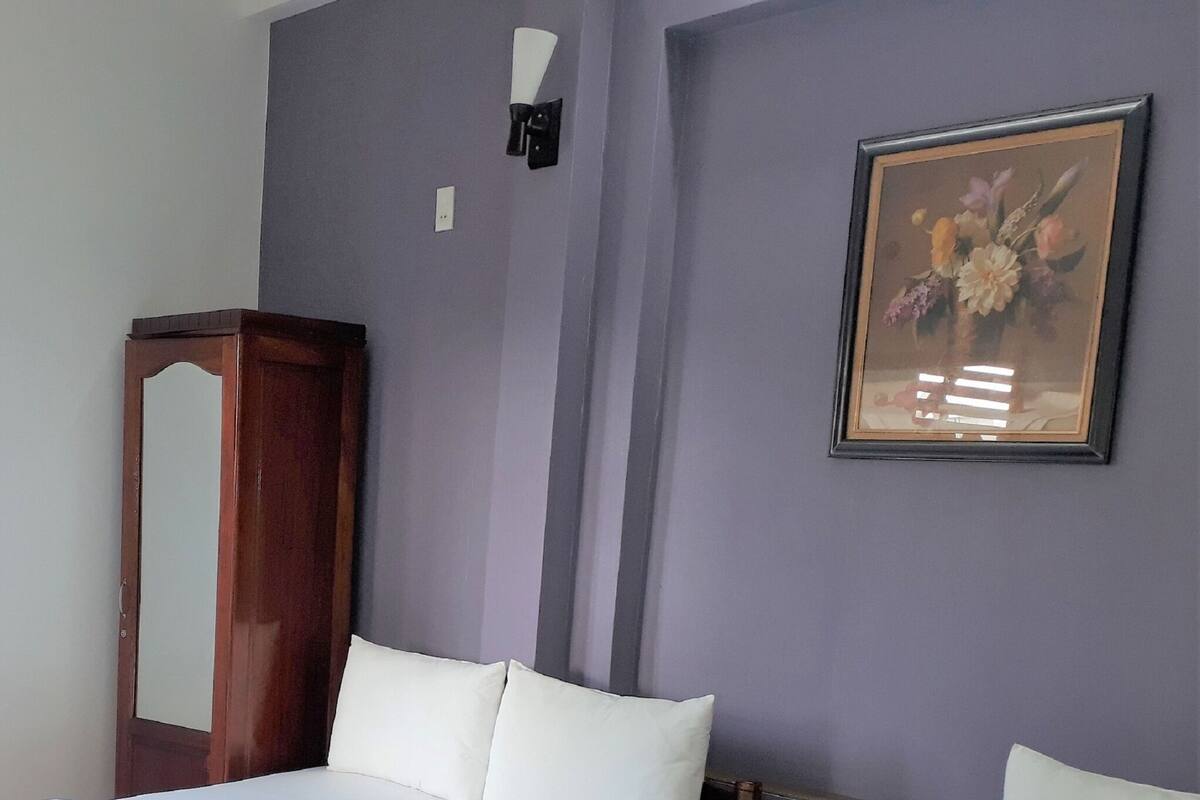 A room with a bed, a mirror, a wall-mounted light, and a framed floral painting.