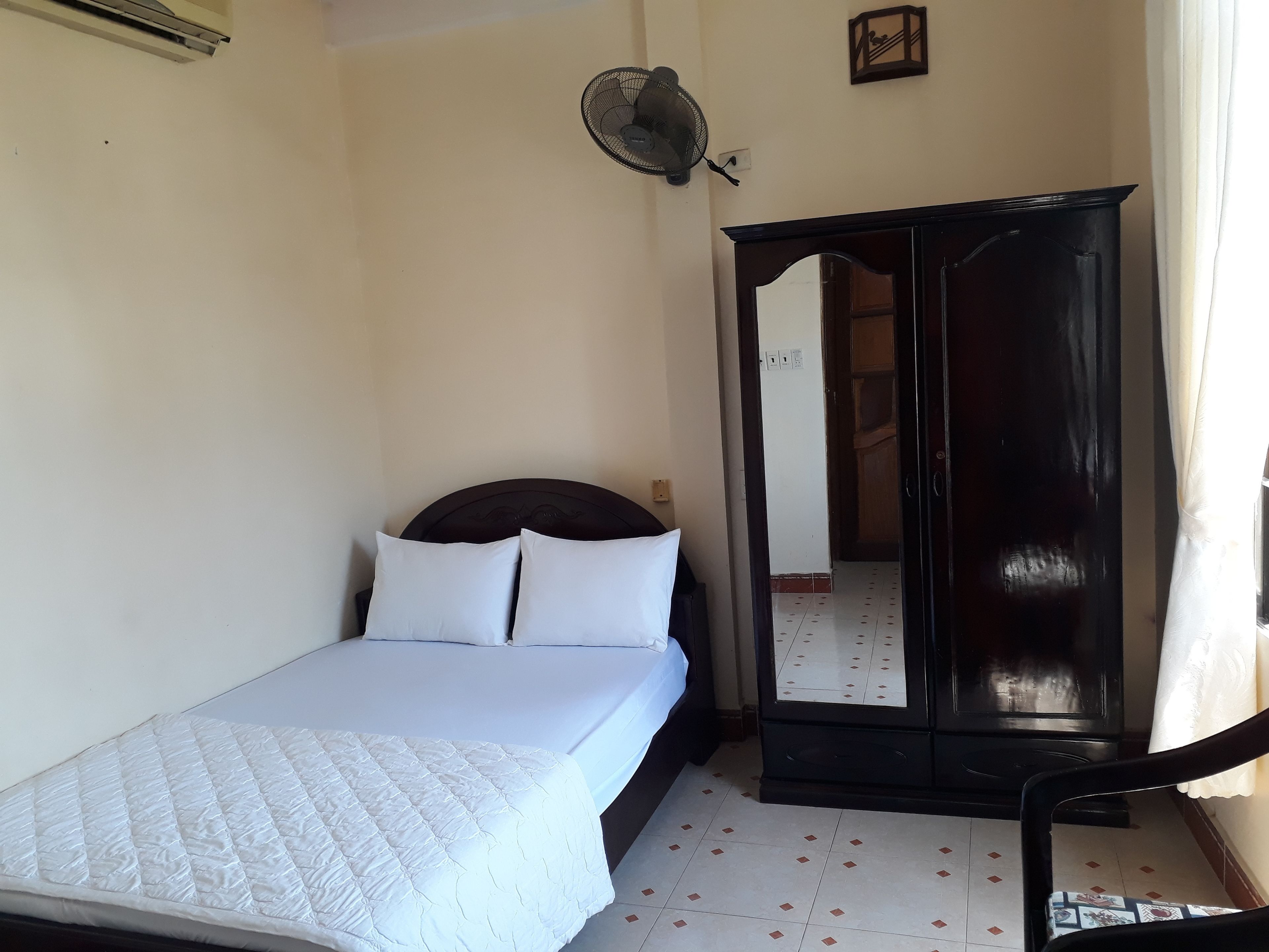 Une chambre à coucher comprenant un lit, une armoire, une chaise et un ventilateur fixé au mur.