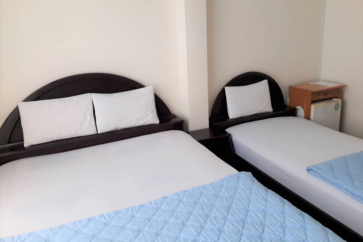 Two single beds with dark headboards and white bedding, a small wooden nightstand with a refrigerator, and a plain wall.