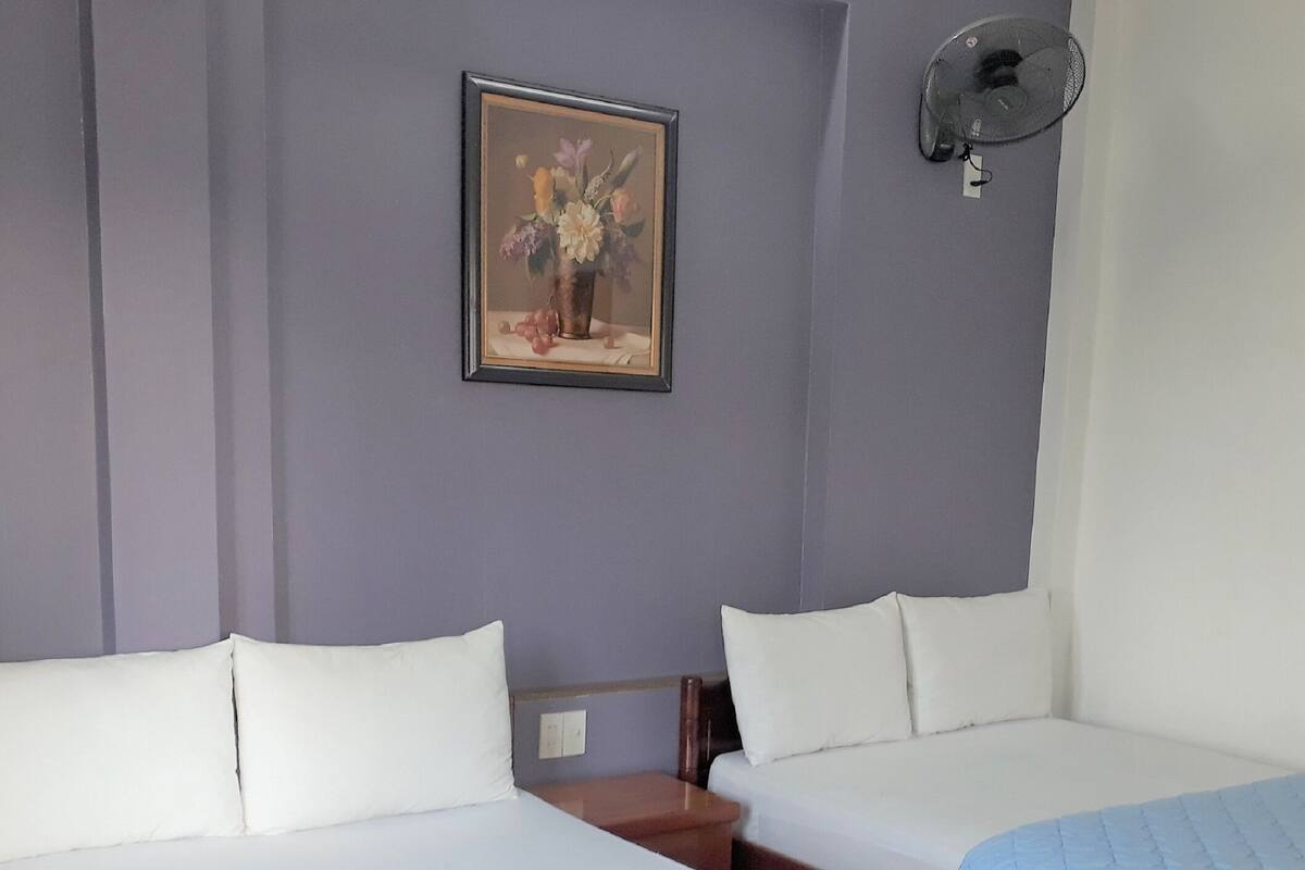 A bedroom with two beds, a framed floral artwork on the wall, and a ceiling fan.