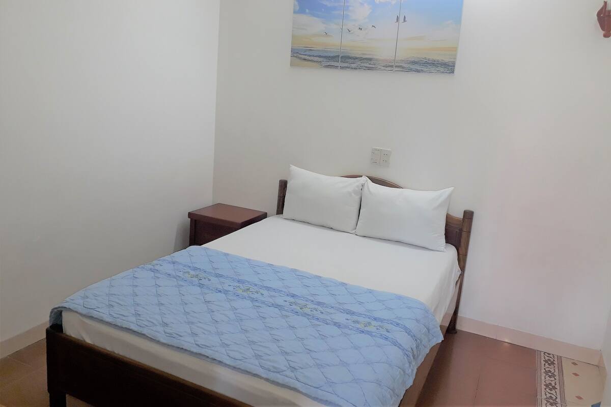 A bedroom with a bed, a nightstand, a wall-mounted painting, and a power outlet.