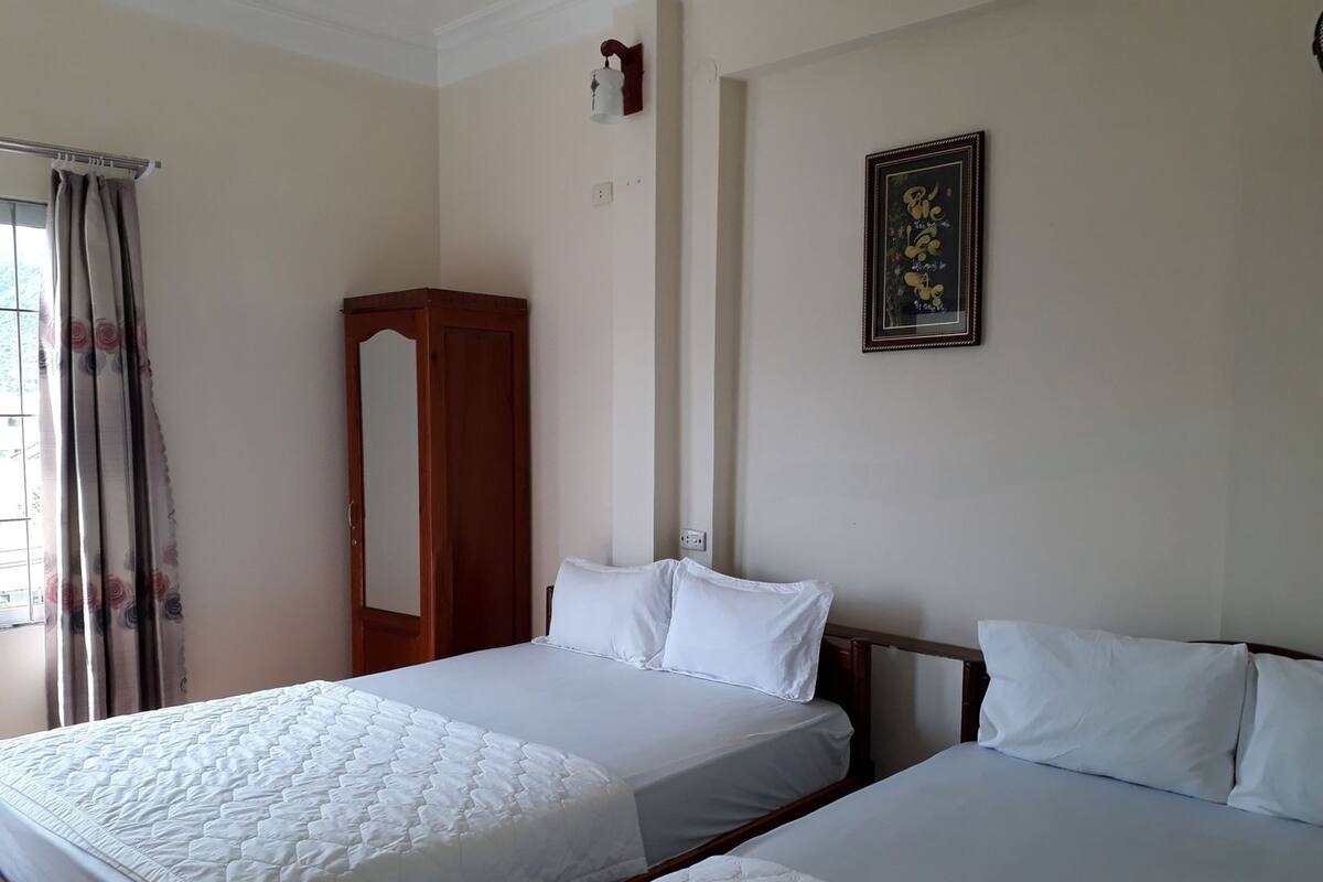 A hotel room with two beds, a wardrobe, a wall-mounted light, and a framed picture.