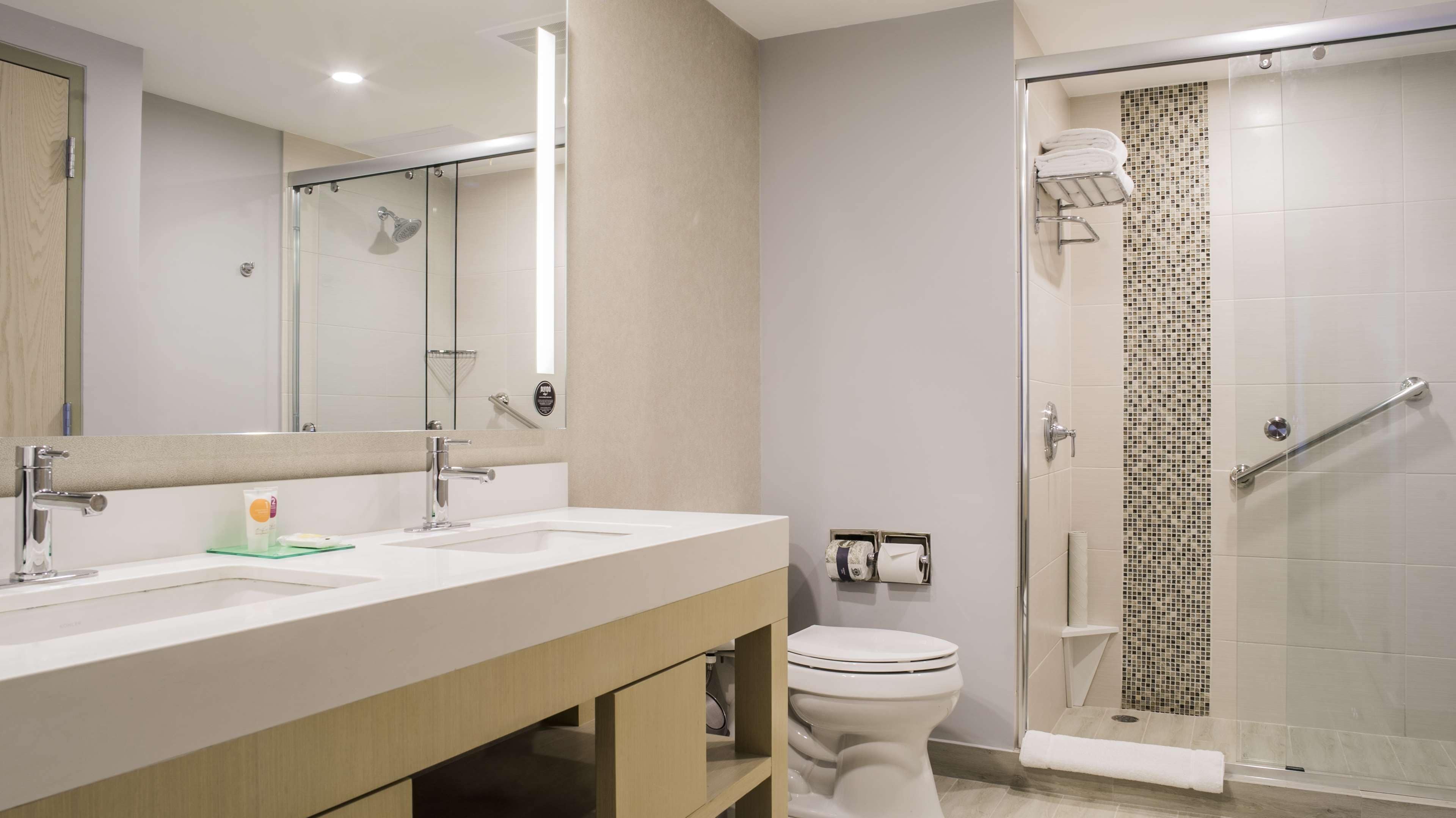 A modern bathroom with two sinks, a toilet, a glass shower enclosure, and a towel rack.