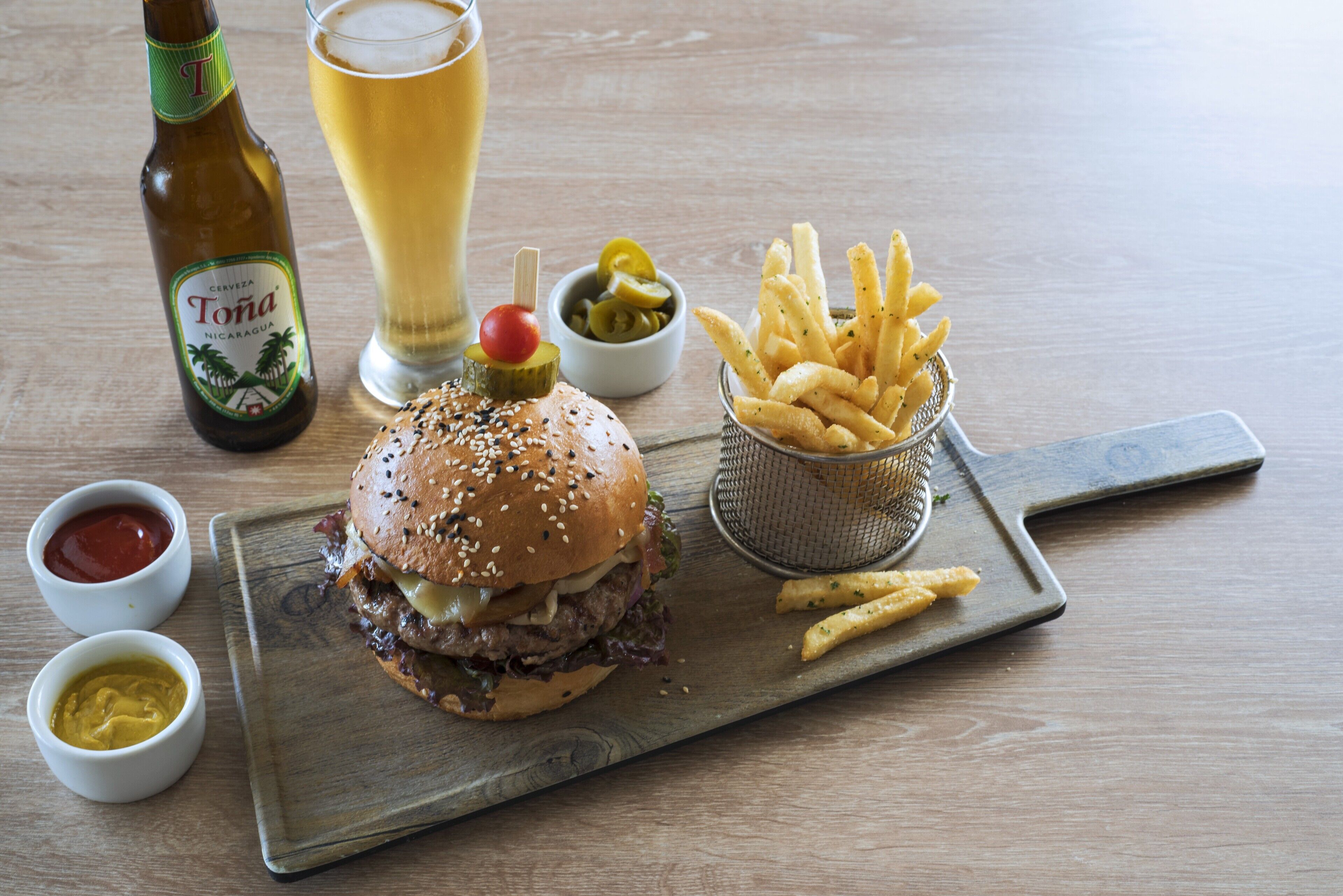 Un repas composé d’un hamburger, de frites et de sauces, le tout servi sur une planche en bois.