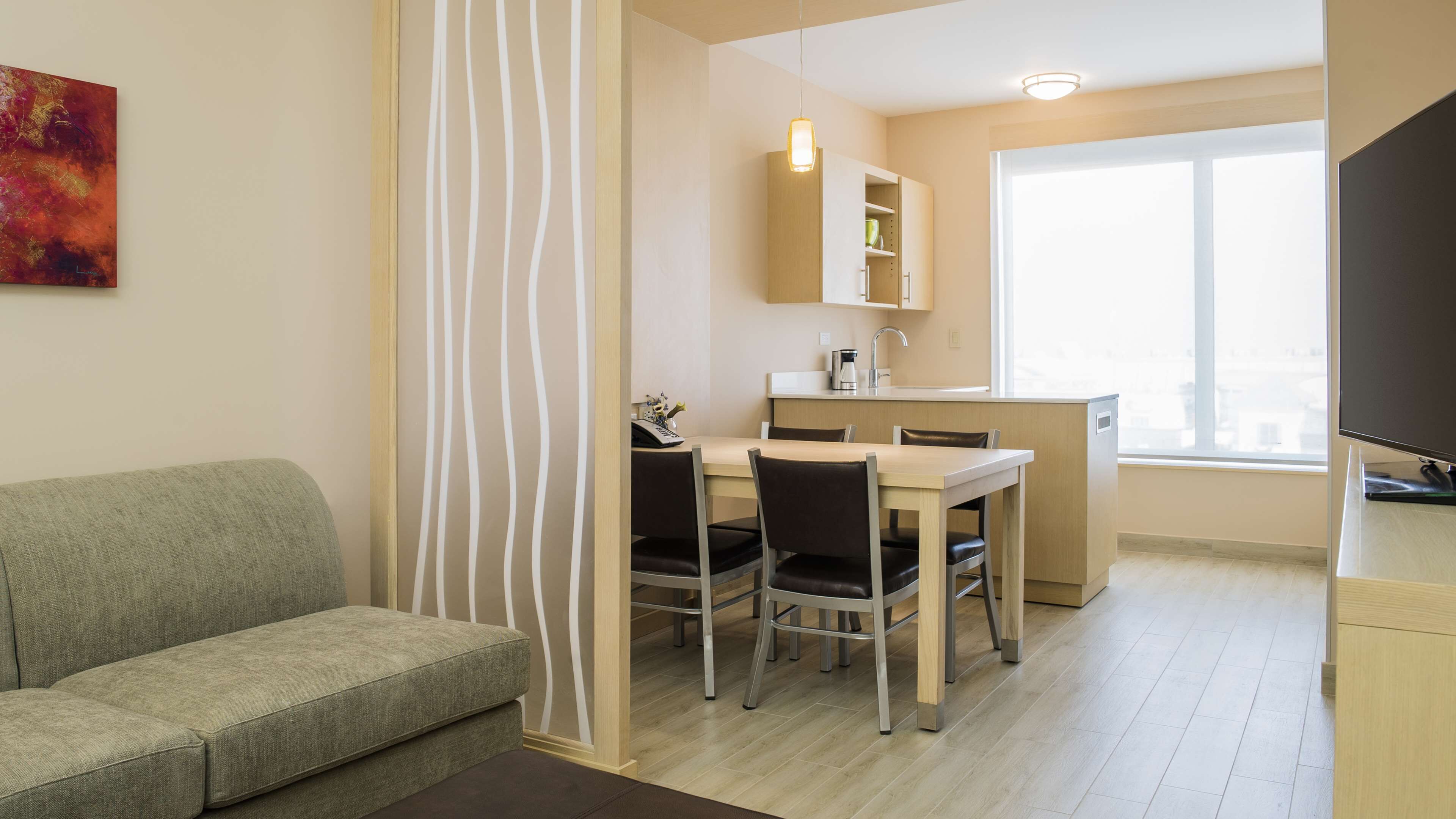 Una sala moderna con sofá, comedor con mesa y sillas, cocina con armarios y pileta, y un ventanal que proporciona luz natural.